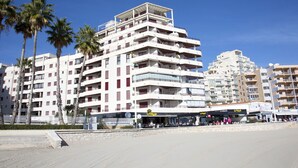 Un hôtel à plusieurs étages doté de balcons, situé près d’une plage bordée de palmiers.