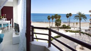 Un balcon avec vue sur la plage, les palmiers et un ciel bleu dégagé.