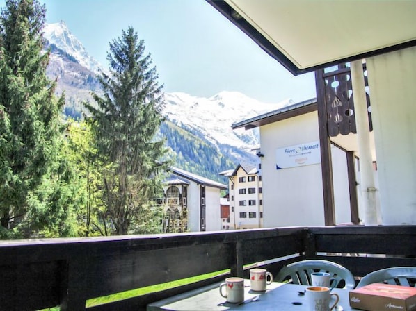 A balcony with a view of snow-capped mountains, a sign for 'Pierre Vacances', and a table with cups and a box.