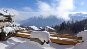 Ein mit Schnee bedeckter Balkon mit Blick auf Berge und einen klaren Himmel.