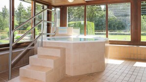 Ein Wellnessbereich mit Whirlpool, einer Treppe und Blick auf einen Garten durch große Fenster.
