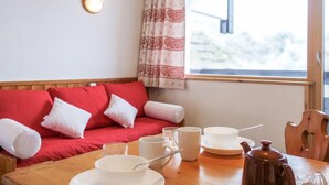 A cozy room with a red sofa, a wooden table with breakfast items, and a window with a view of trees. - Home Club (Lavachet) by Interhome (Tignes)