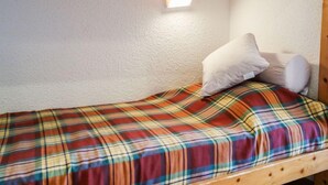 A single bed with a plaid bedspread and two pillows in a room with white walls and a wooden ceiling beam. - Home Club (Lavachet) by Interhome (Tignes)