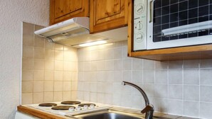 A compact kitchen with a stove, sink, and wooden cabinets. - Home Club (Lavachet) by Interhome (Tignes)