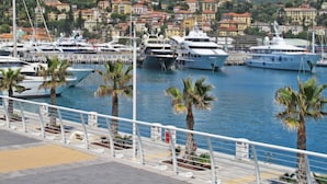 Una marina con yacht ormeggiati, palme e una collina sullo sfondo con edifici colorati.