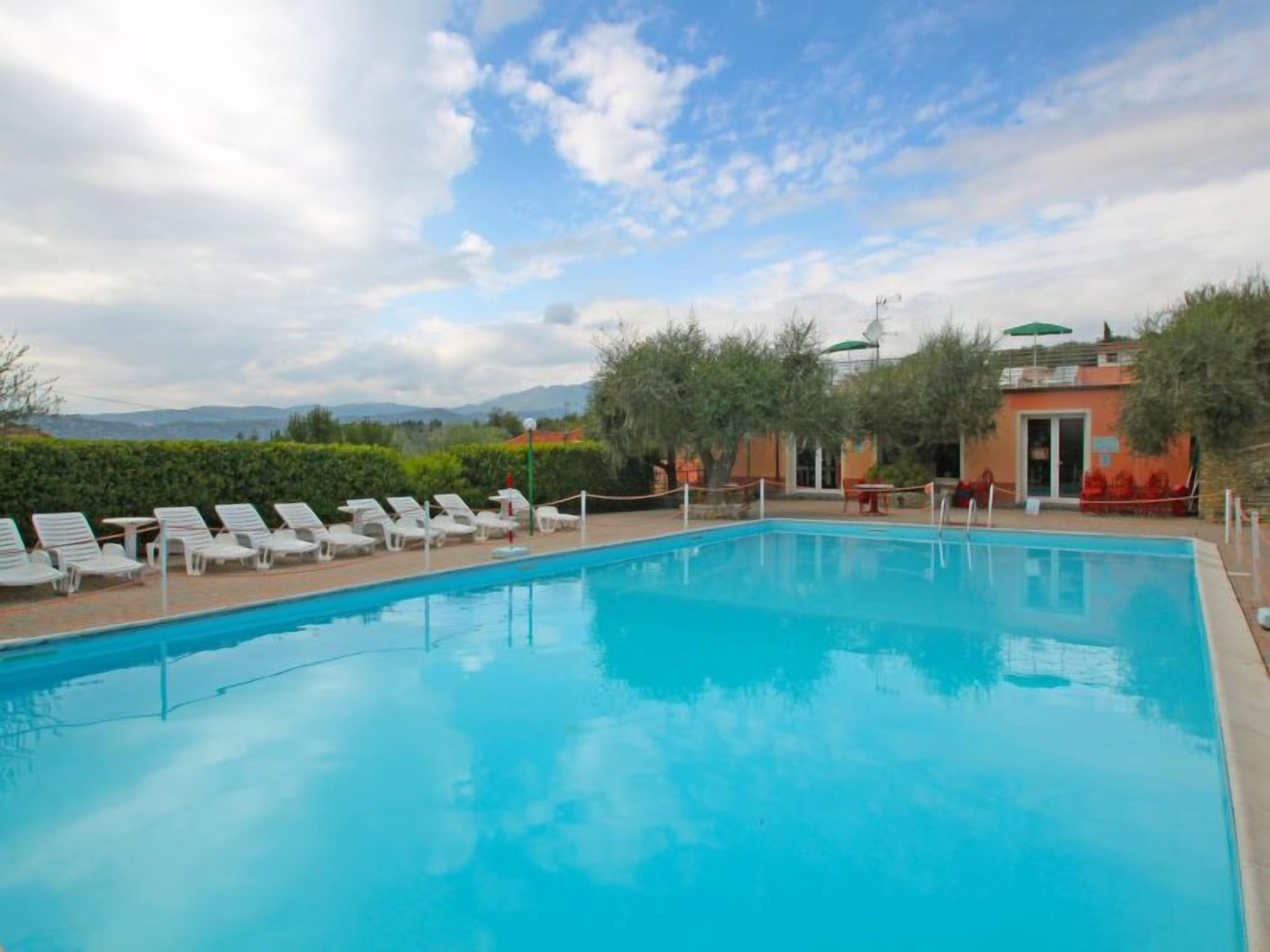 Ein Swimmingpool mit Liegestühlen, ein Gebäude mit rotem Dach und eine gebirgige Kulisse.