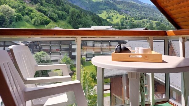 Un balcone con vista su un paesaggio montuoso, un tavolo con un vassoio e una sedia bianca.