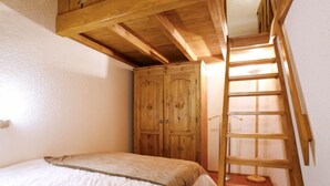 Una camera da letto con un letto in legno, un armadio e una scala di legno che conduce a una zona mansardata.