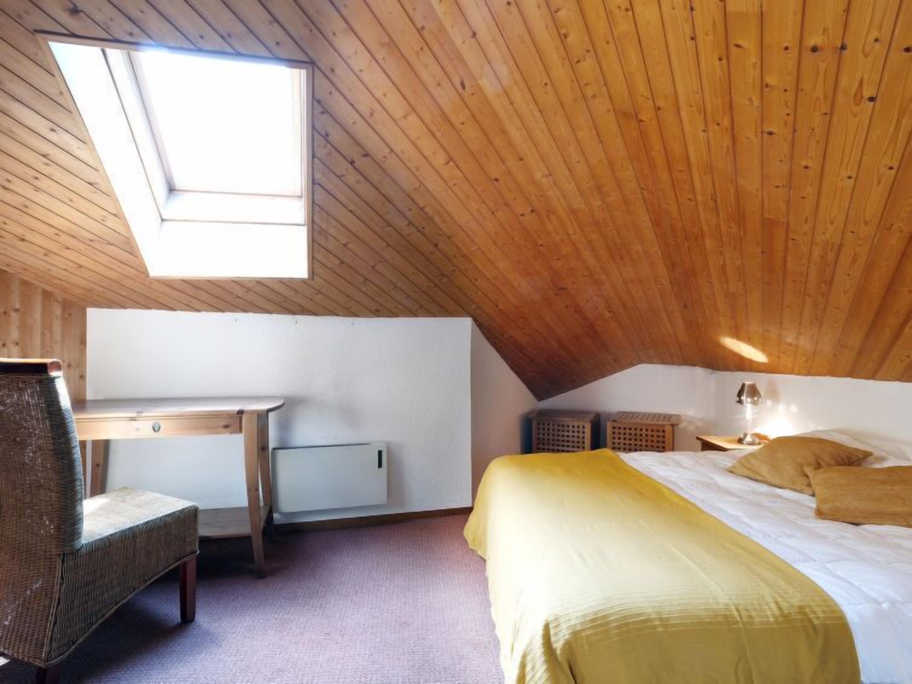 A cozy attic bedroom with a sloped ceiling, a bed with yellow bedding, a desk with a chair, and a skylight.