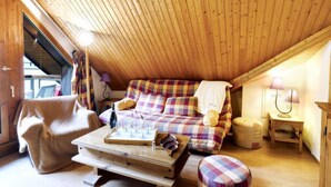 Una camera da letto mansardata accogliente, con un soffitto spiovente in legno, un letto a quadri, una panca di legno e un tavolino con dei bicchieri.