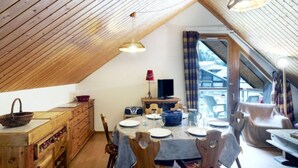 Accogliente zona pranzo in mansarda, con soffitto in legno, un tavolo da pranzo per quattro persone e una televisione su un mobile.