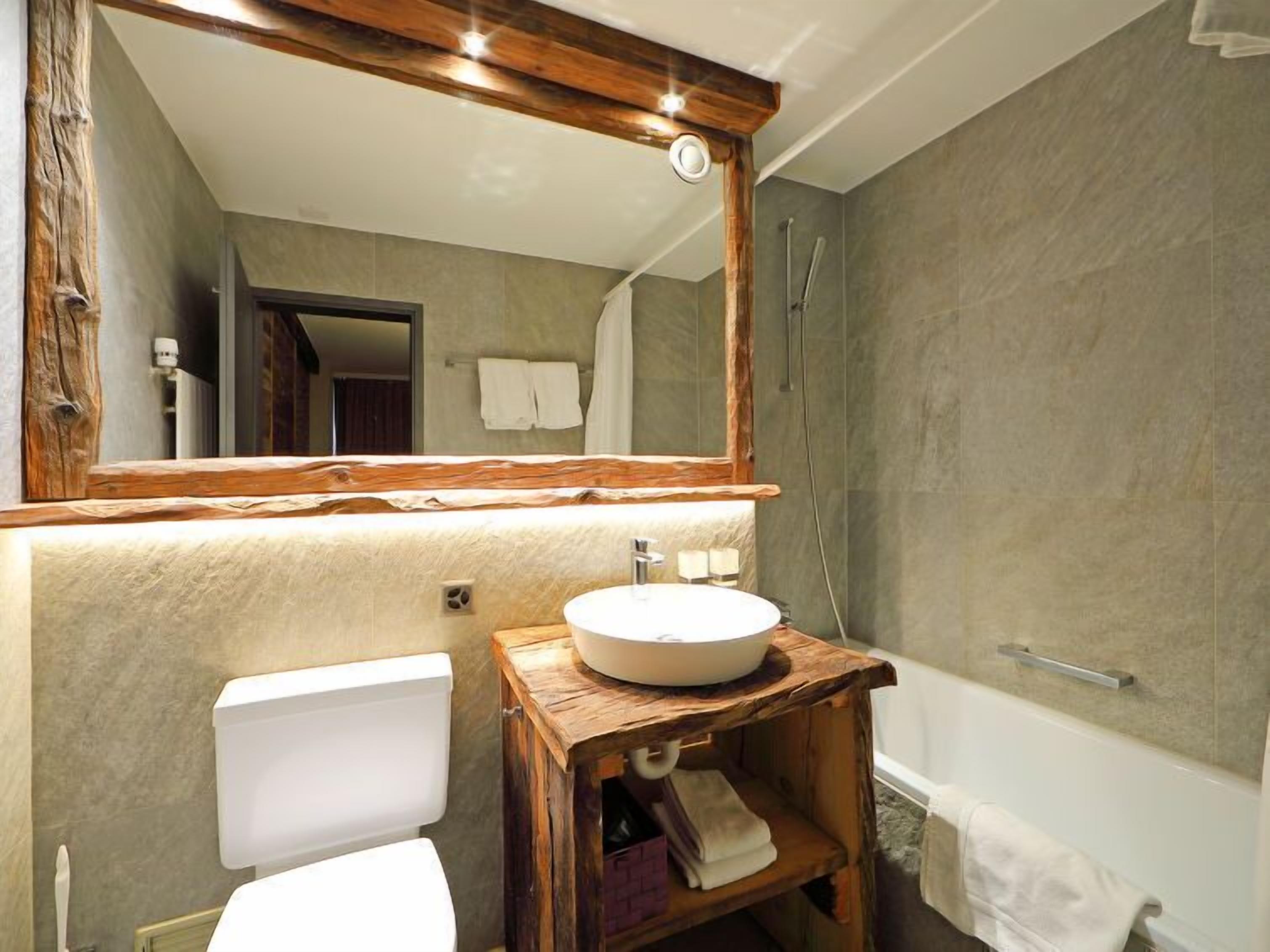 A bathroom with a wooden vanity, a white sink, a toilet, a bathtub, and a large mirror.