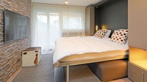 A modern bedroom with a stone accent wall, a large bed with polka dot pillows, and a flat-screen TV mounted on the wall. - Grillon by Interhome (Zermatt)