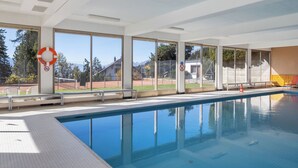 A swimming pool with clear views of the outdoors, including a tennis court and a mountain in the background.