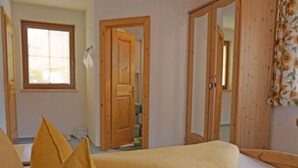 Une chambre avec deux lits, des portes en bois, une fenêtre et un miroir.