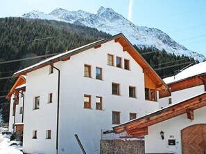 A two-story building with a white facade and wooden accents, set against a backdrop of snow-capped mountains. - Christina by Interhome (Pettneu am Arlberg)