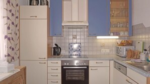Une cuisine compacte avec des meubles blancs, un four encastré, un four à micro-ondes et une machine à café.