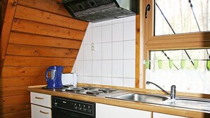 A compact kitchen with wooden walls, a white tiled backsplash, a black dishwasher, and a sink with a green window view. - Nepumuk by Interhome (Arendsee)