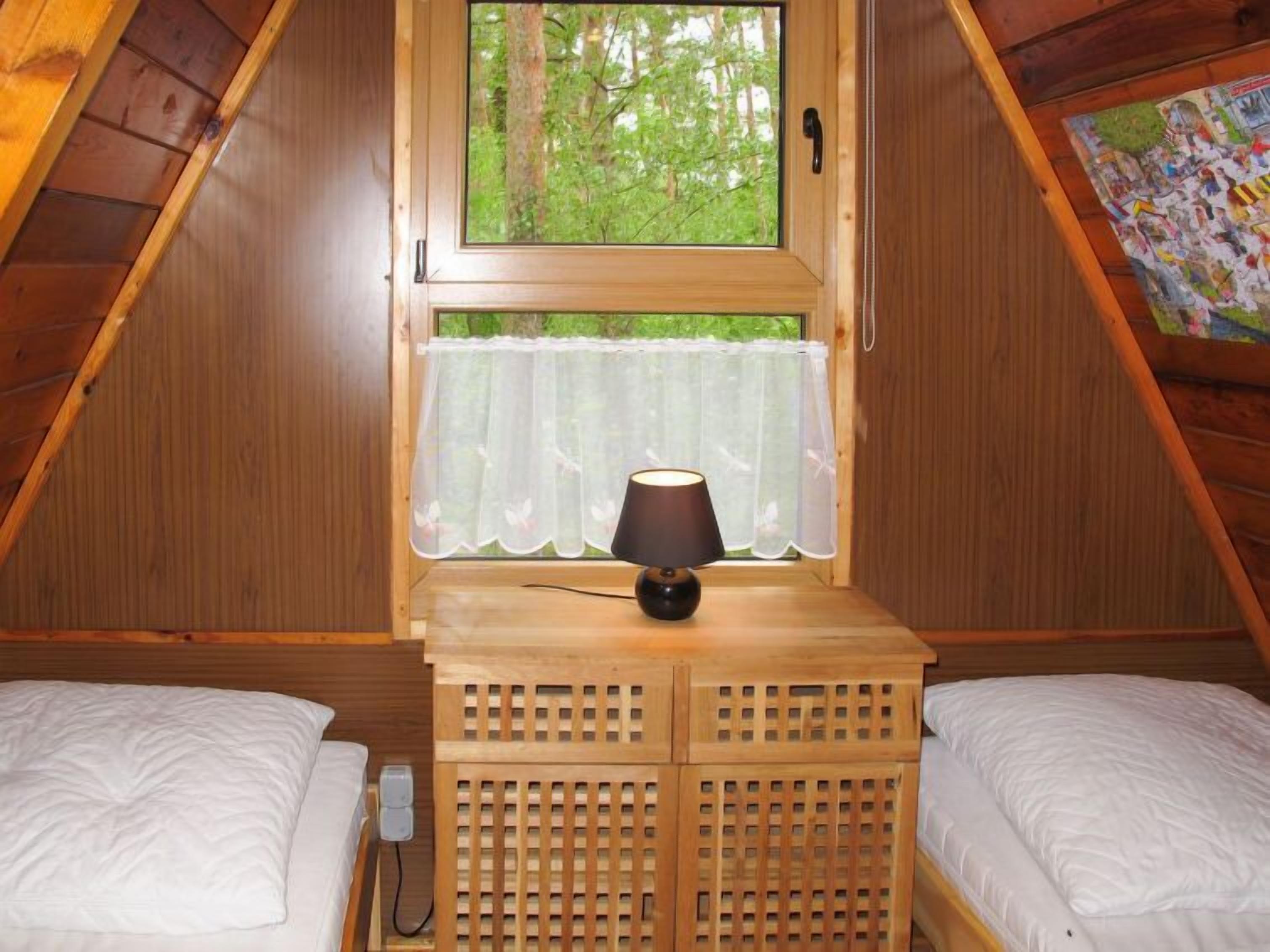 A cozy room with two beds, a window with a view of trees, and a lamp on a wooden table.