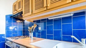 A kitchen with blue tiles, wooden cabinets, a white sink, and a dish rack. - Galiote by Interhome (Cogolin)