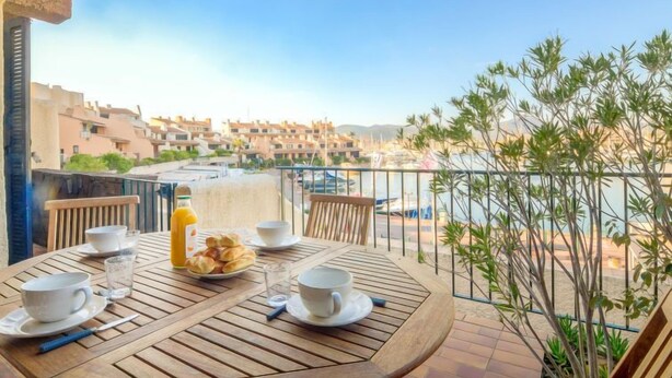A wooden table set with white cups, saucers, and a bottle of orange juice, overlooking a marina and coastal buildings. - Galiote by Interhome (Cogolin)