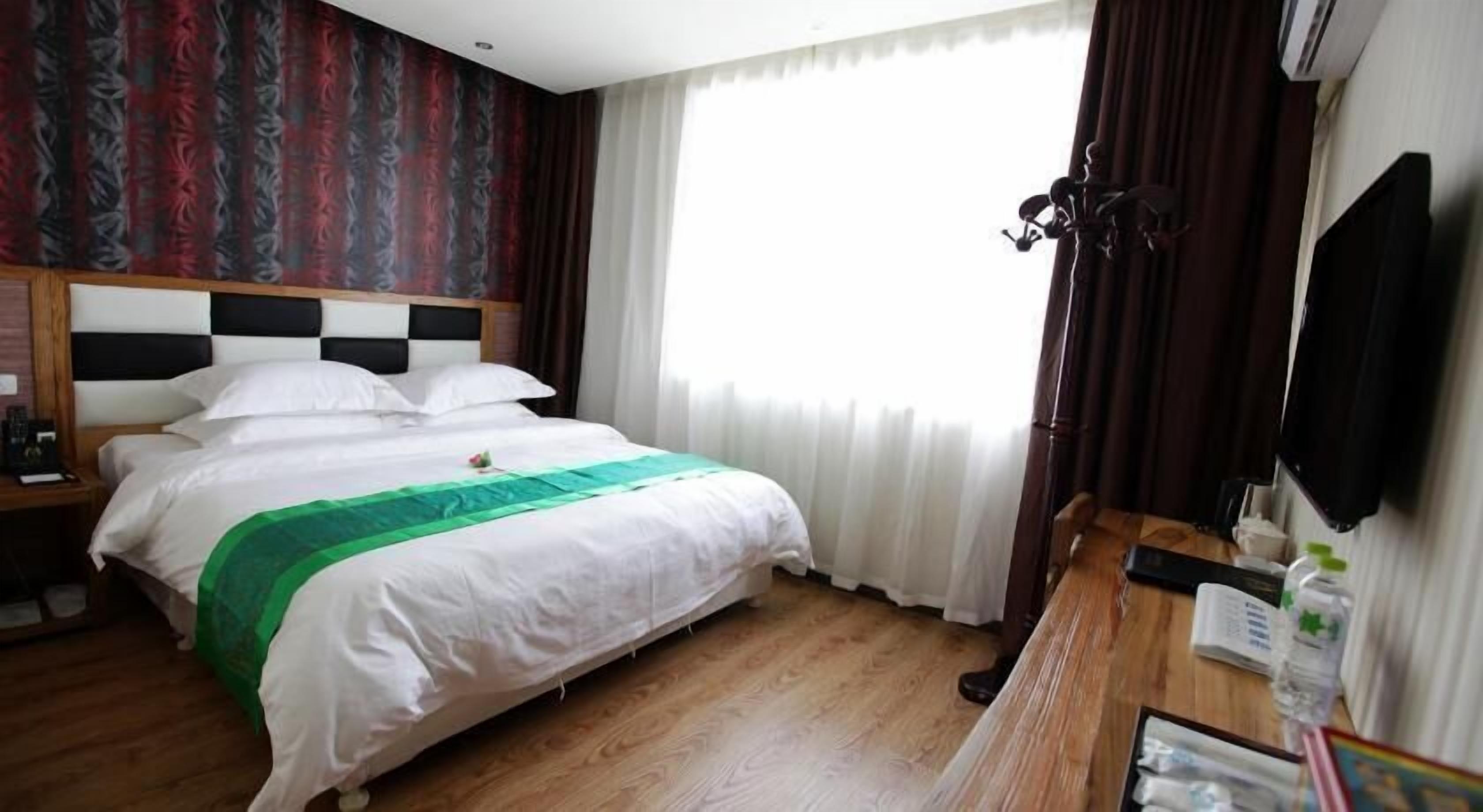 Hotelkamer met een bed, een houten nachtkastje, een bureau met stoel, een flatscreen-televisie aan de muur en een raam met gordijnen.