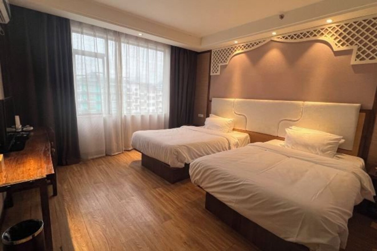 Una habitación de hotel con dos camas, un escritorio de madera y un ventanal con cortinas.