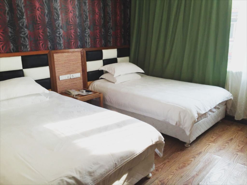 Une chambre d’hôtel avec deux lits simples, une tête de lit en bois, une table de chevet avec un téléphone et un rideau vert.