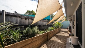 Un jardín con jardineras de madera, un sendero de grava y una cerca azul.