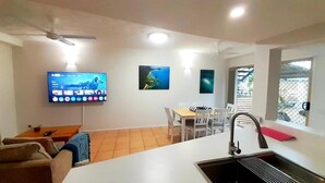 Una cocina moderna con comedor, televisor montado en la pared y ventilador de techo.