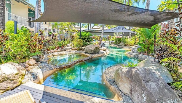 Zona de piscina con agua cristalina, rodeada de rocas y plantas tropicales.