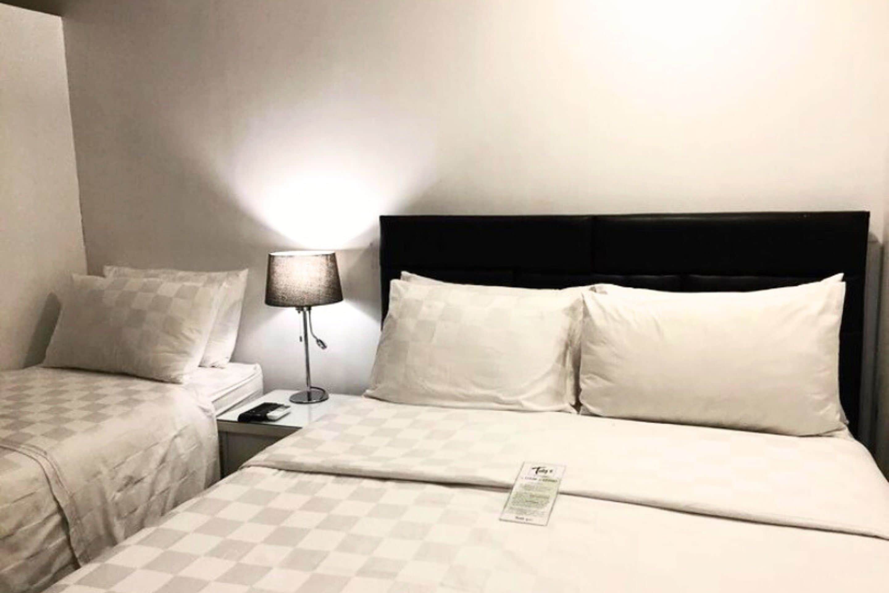 A hotel room with two beds, a nightstand, a lamp, and a visible room number.