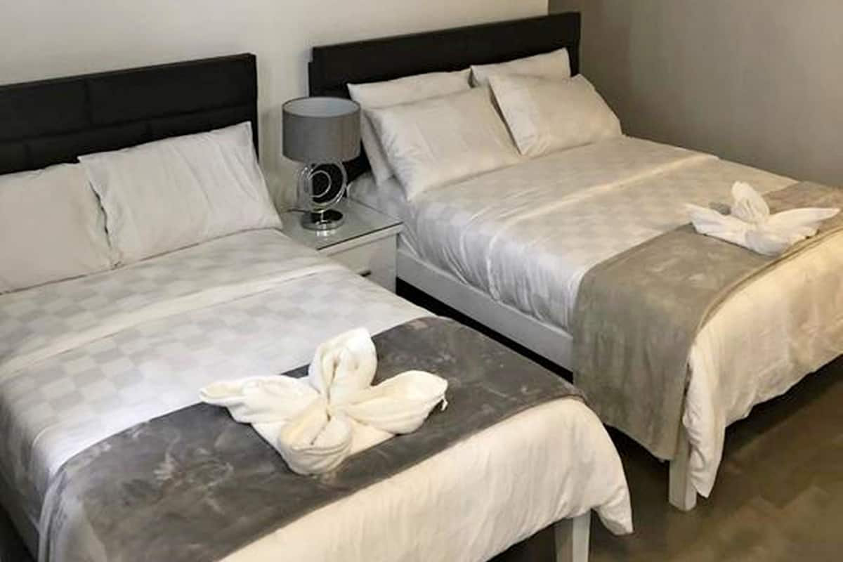 Habitación de hotel con dos camas, cada una con una almohada y una toalla. Hay una mesita de noche con una lámpara y un objeto decorativo pequeño.