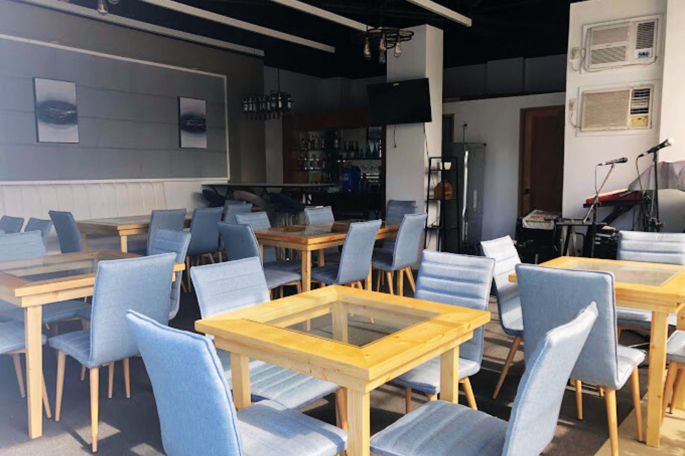 A restaurant with multiple tables and chairs, a bar area, and a stage with musical equipment.