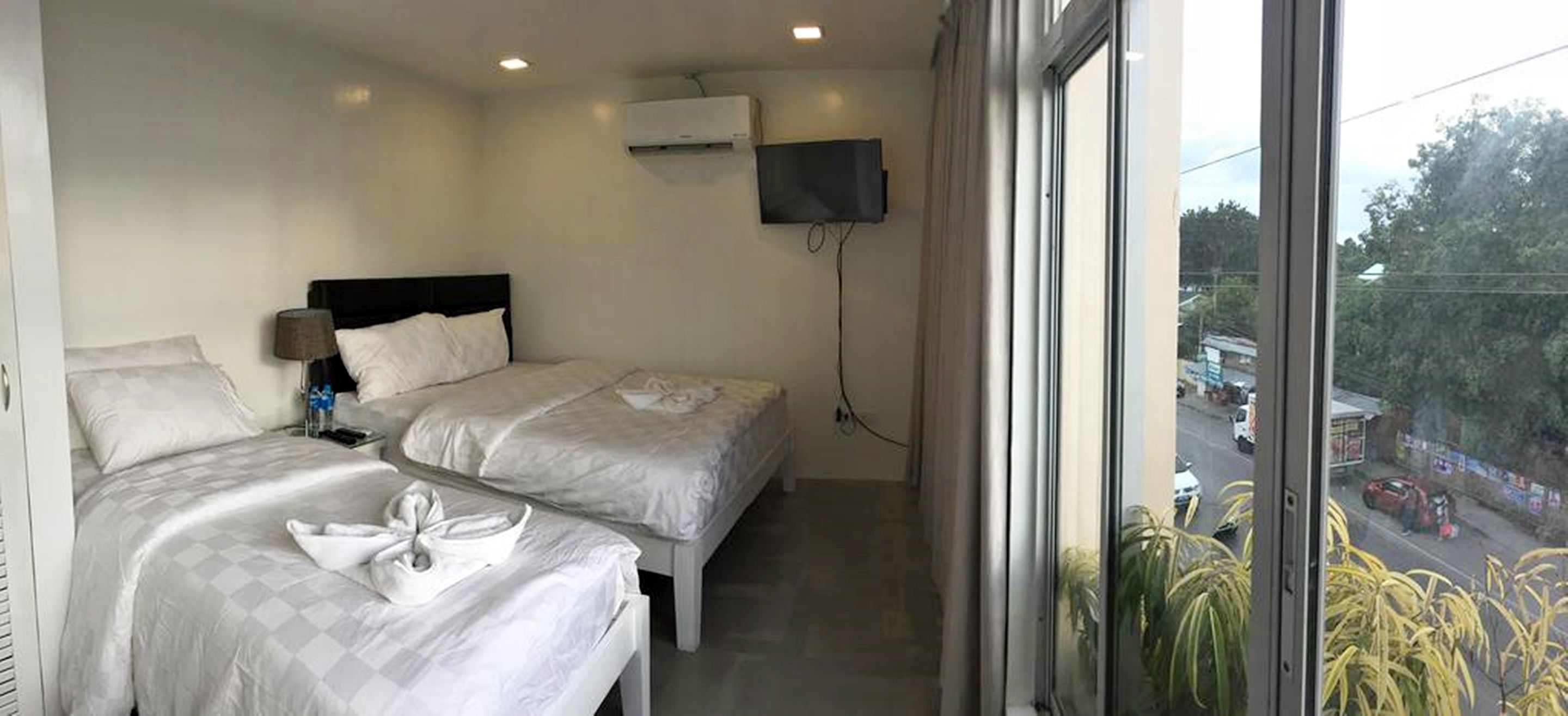 A hotel room with two beds, a TV mounted on the wall, and a window overlooking a street.