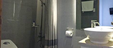 A modern bathroom with a glass-enclosed shower, a toilet, a sink with a mirror, and a trash bin.