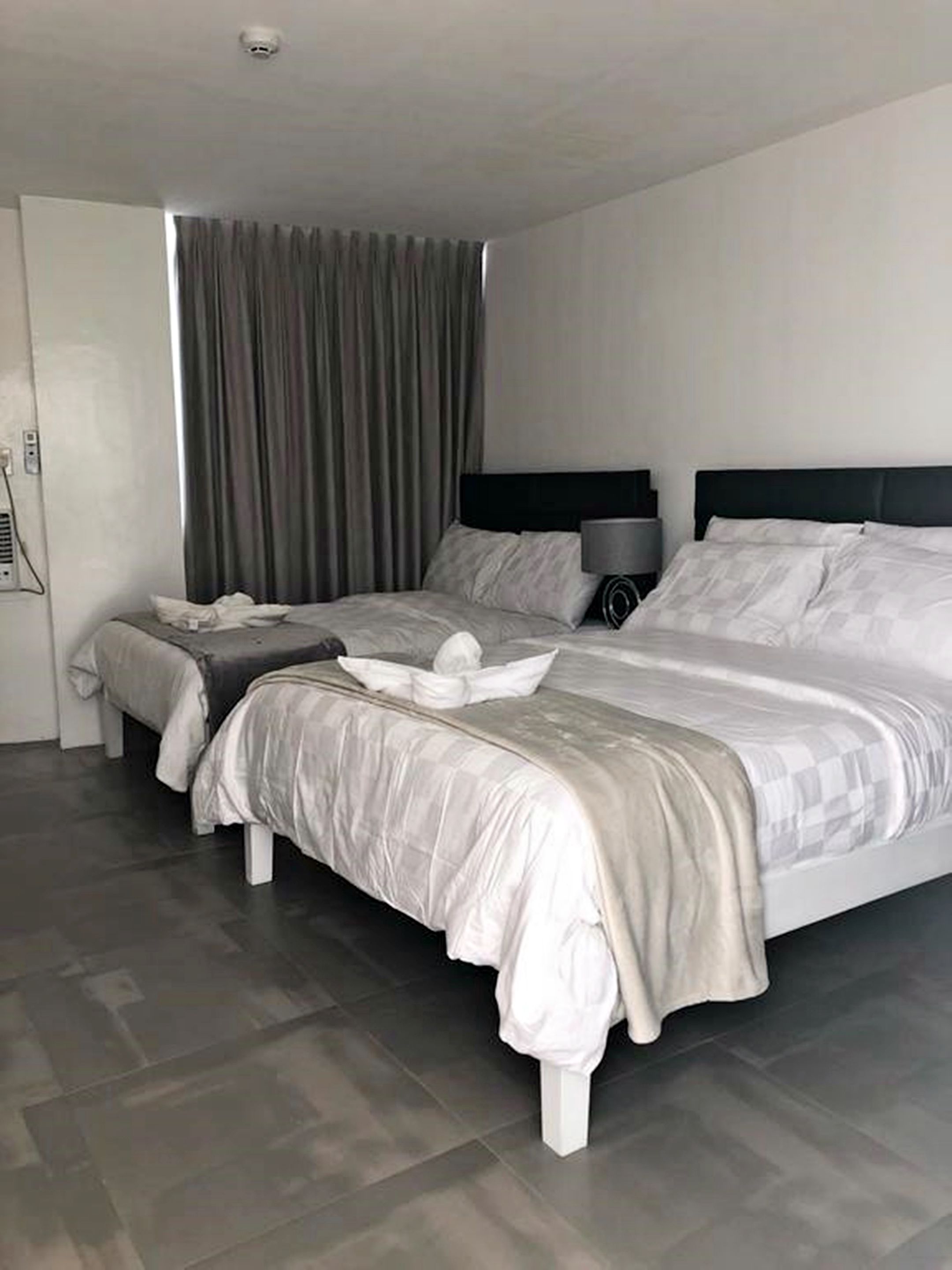 Una habitación de hotel moderna con una cama grande, dos mesitas de noche y una ventana con cortinas.