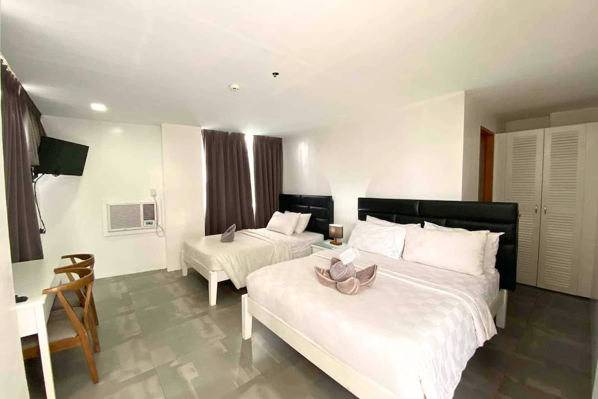 Habitación de hotel con dos camas, un escritorio, una silla, un televisor y un armario.