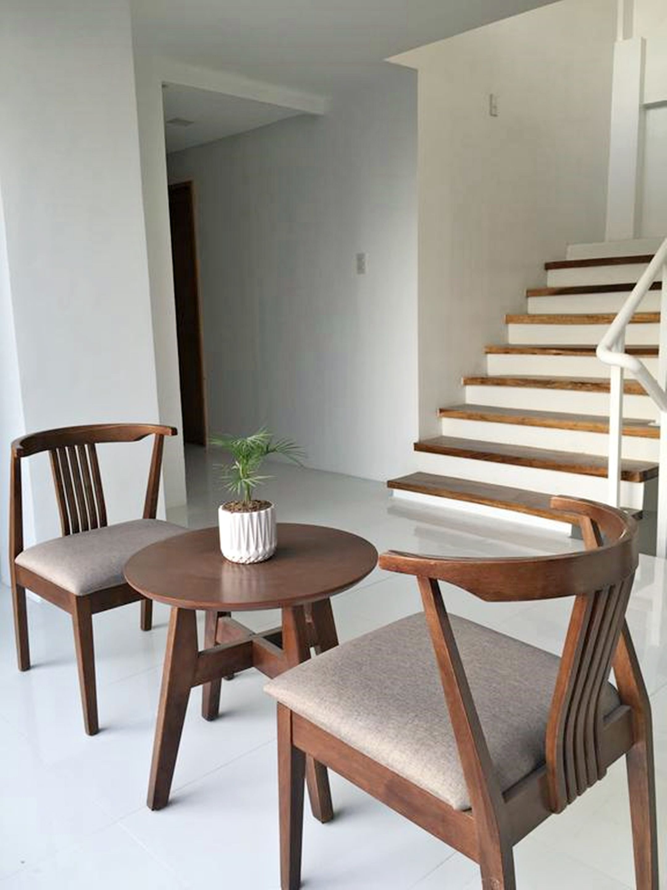 A modern interior with a staircase, two wooden chairs, a round table, and a potted plant.