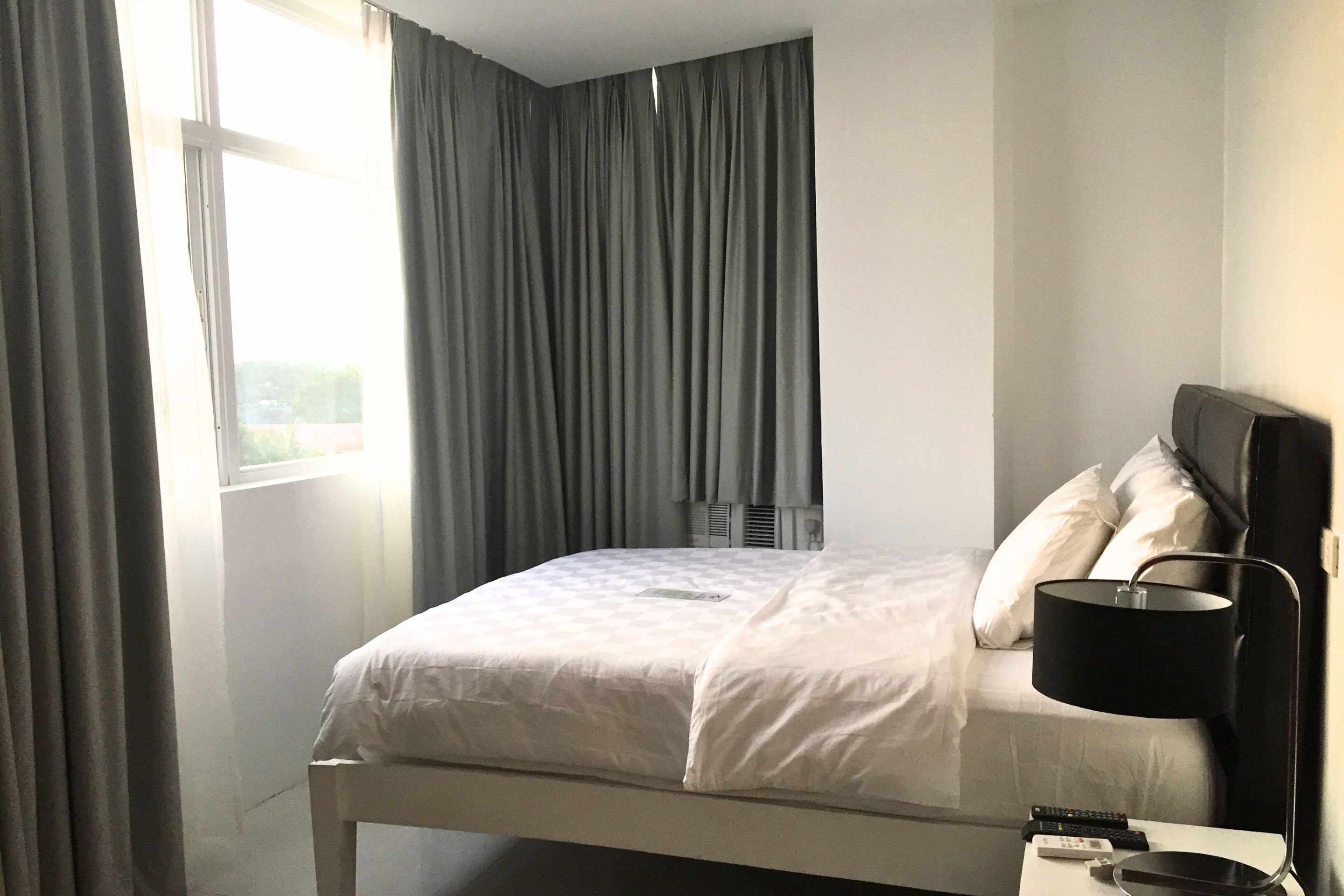 A hotel room with a bed, a nightstand, a lamp, and a window with curtains.