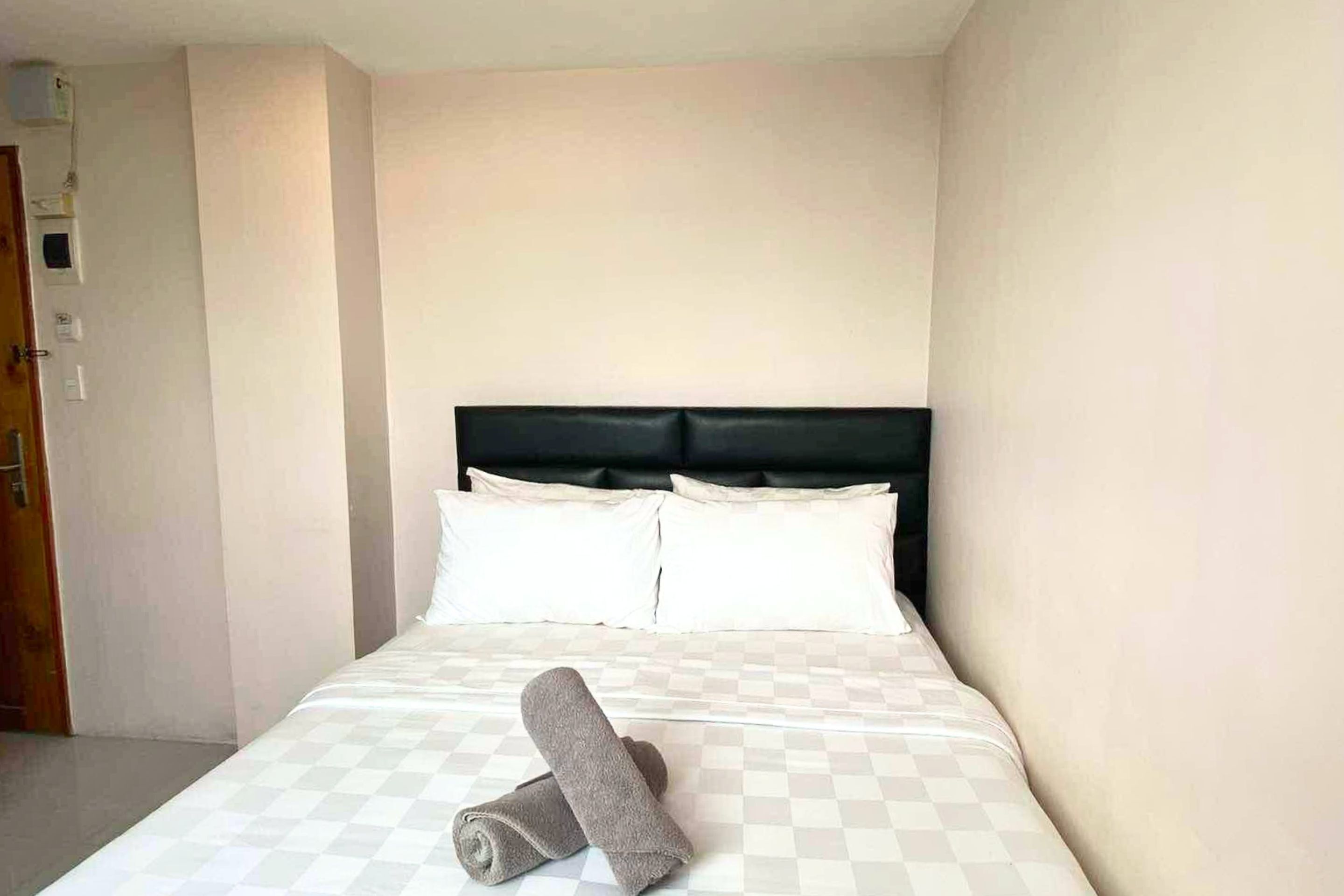 Ein ordentlich bezogenes Bett mit einer karierten Tagesdecke, zwei Kissen und einem aufgerollten Handtuch.