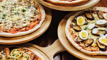 Quatre pizzas, présentées sur des planches en bois, chacune garnie d’ingrédients différents, sont disposées sur une table.