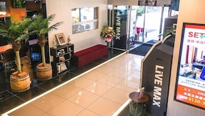 Rebedor d'hotel amb una taquilla d'informació, un sofà vermell, plantes en testos i un cartell que diu 'LIVE MAX'.