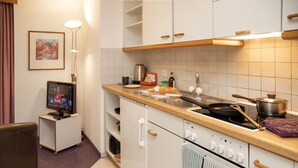 Eine kleine Küche mit weißen Schränken, einem Siemens-Kochfeld, einer Spüle und einem Fernseher in der Ecke.