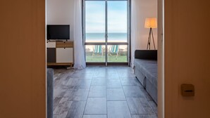 A hotel room with a large sliding glass door to the beach, a TV on a wooden desk, and a lamp on the right. - Les Caravelles by Interhome (Cabourg)