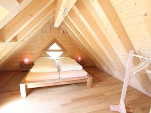 A cozy attic bedroom with a wooden sloped ceiling, a bed with two pillows, and a nightstand with a lamp. - Apartment Lärche by Interhome (Grosserlach)