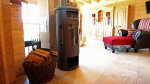A cozy log cabin interior with a wood-burning stove, a wicker basket, a leather sofa, and wooden cabinets. - Apartment Lärche by Interhome (Grosserlach)