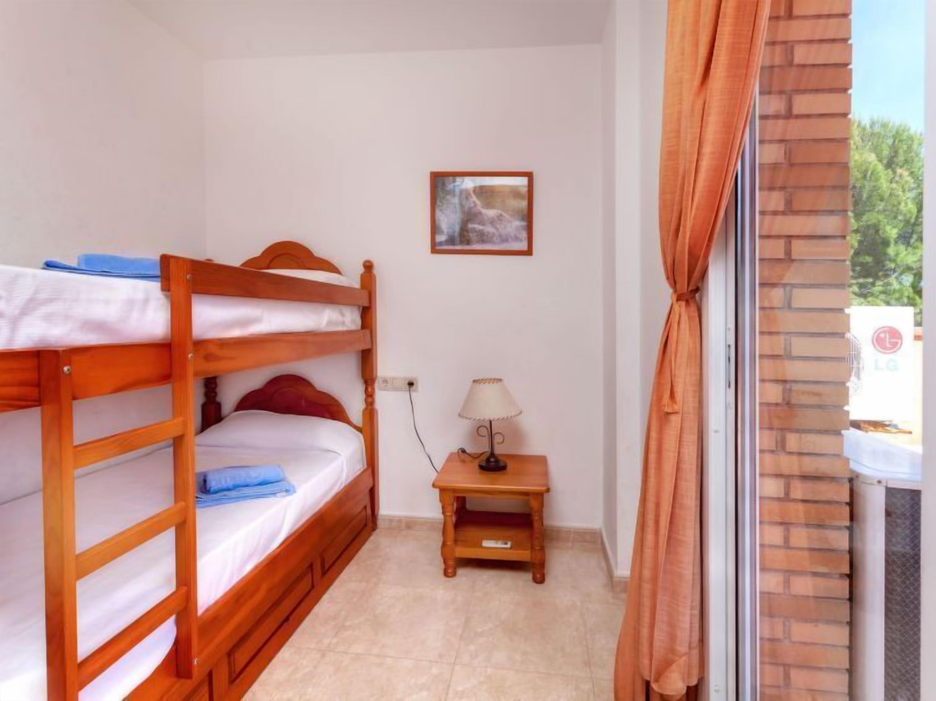 Una stanza con un letto a castello, un tavolino con una lampada, un quadro appeso al muro e vista dalla finestra con tende.