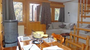 L’intérieur chaleureux d’un chalet avec une table à manger dressée pour deux personnes, une cheminée et un canapé en arrière-plan.