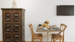 A dining area with a wooden table set for two, a cabinet with horse figures, and a television mounted on the wall. - Double Room Modern by Interhome (Ascona)